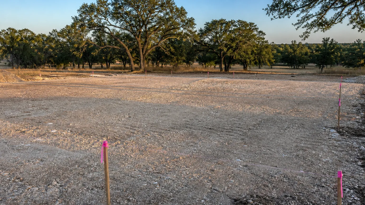 Freshly cleared building pad on oak acreage with survey stakes and string lines at morning