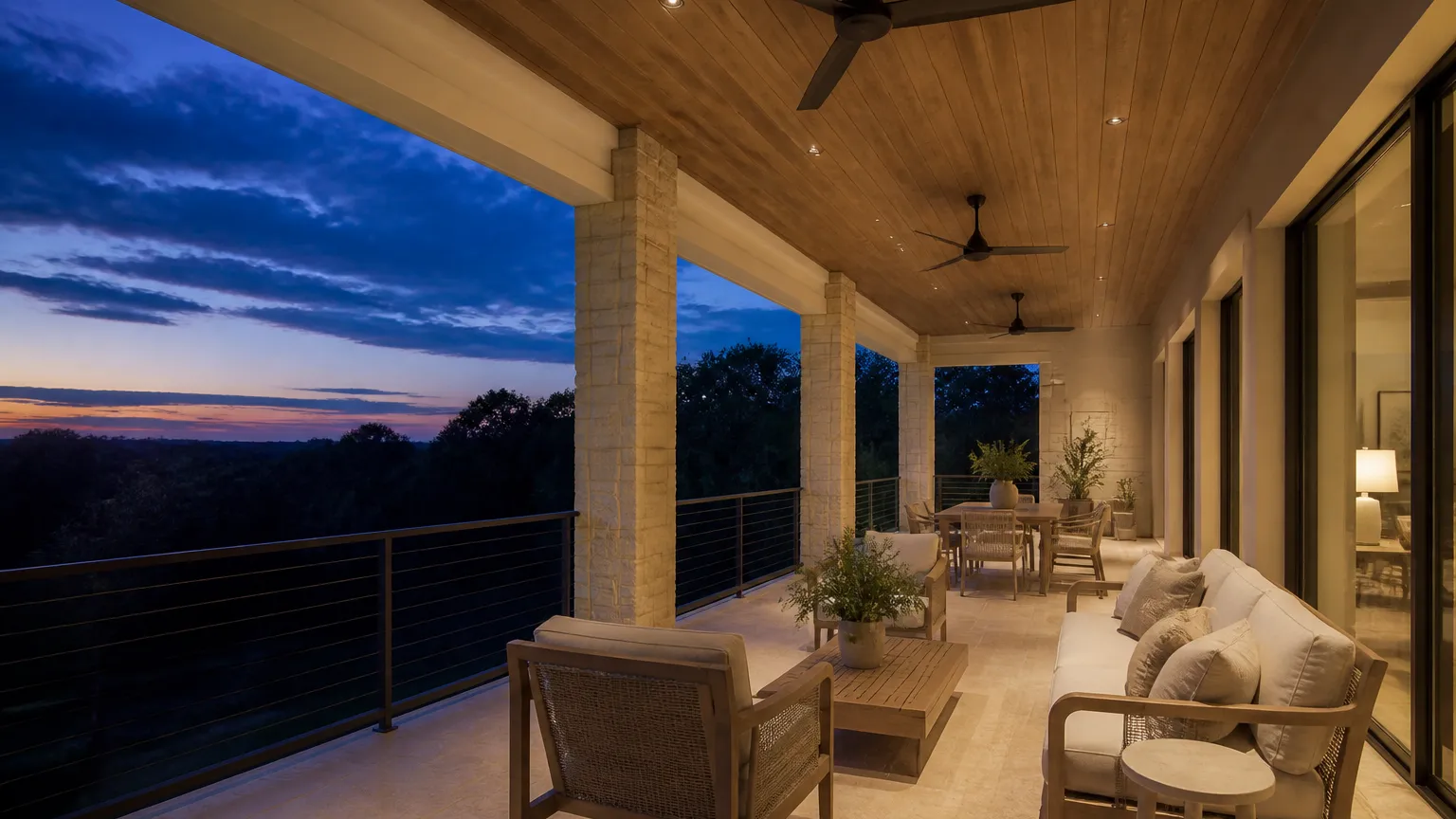Deep covered back porch at dusk with wood ceiling, fans, and limestone columns overlooking dark oaks