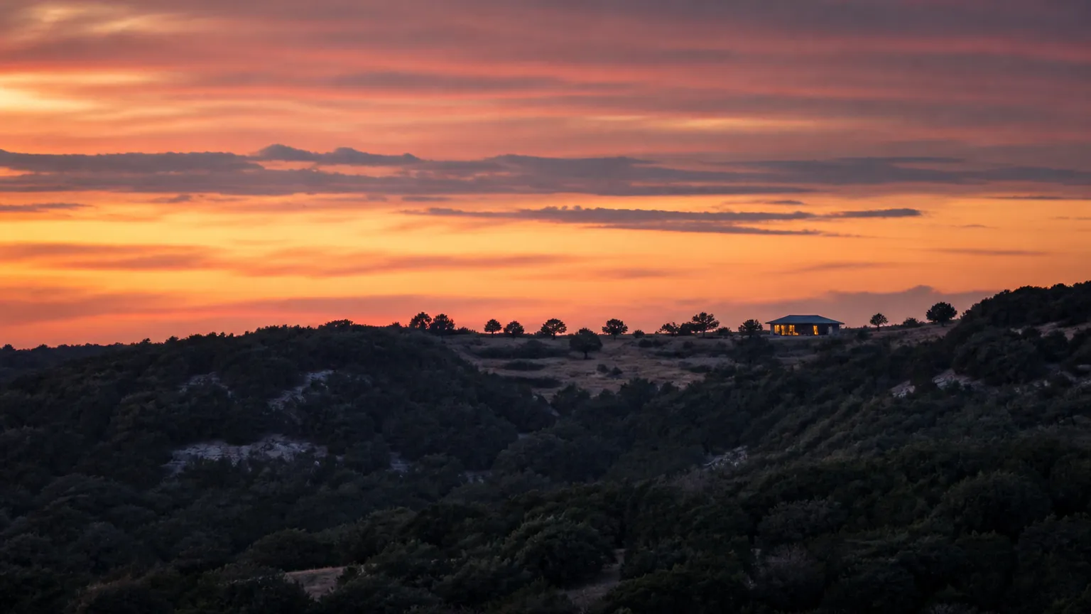 Hill Country ridge at sunset with a distant home showing softly glowing windows
