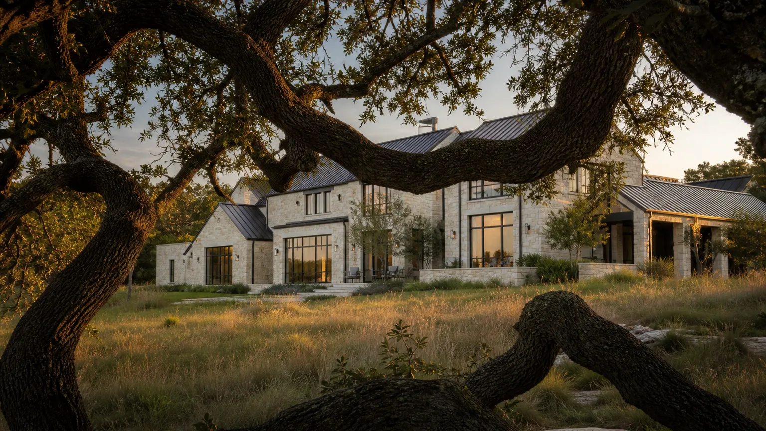 Completed limestone custom home framed by massive live oak branches in evening light